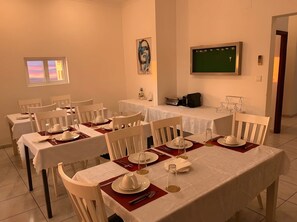 A dining area with tables set for four, white chairs, and a green chalkboard on the wall. - Natalia Guest House (Luanda)