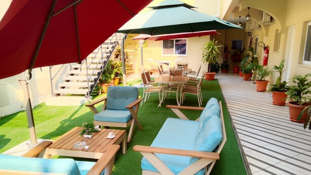 An outdoor patio with wooden furniture, green artificial grass, and potted plants. - Natalia Guest House (Luanda)