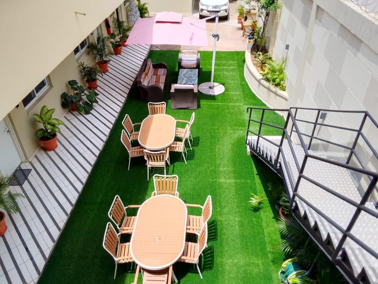 Un patio exterior con varias zonas de estar, incluyendo mesas y sillas redondas, rodeado de plantas en macetas y un pequeño jardín.