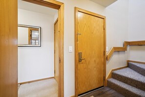 A wooden door with a brass handle, a mirror on the wall, and a carpeted floor.