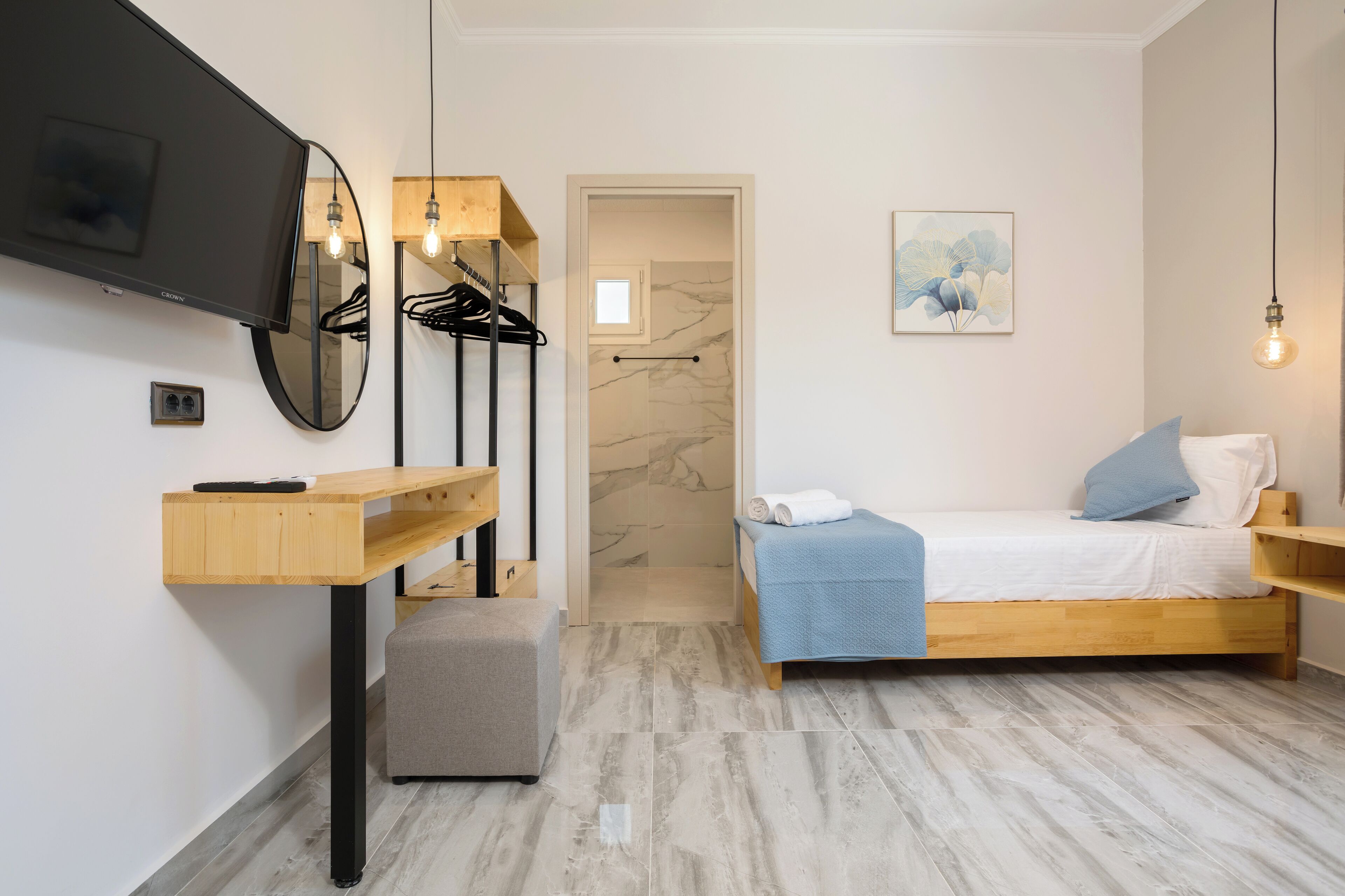 A bedroom with a bed, a desk, a mirror, a TV, and a shower area.