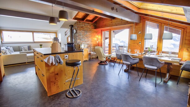 Una cocina amplia con una isla central, taburetes de madera y un comedor con sillas modernas.
