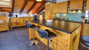 Cocina con armarios de madera, encimera negra y tres taburetes de bar.