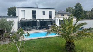 Ett modernt hus i två våningar med en swimmingpool, en uteplats och en välskött gräsmatta.
