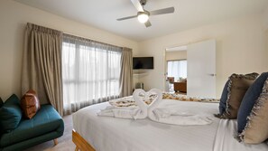A hotel room with a bed, a TV, a ceiling fan, and a view of the outside through the window. - Brothers of Bright.. (Bright)