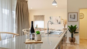 A modern kitchen with a central island, stainless steel appliances, and a dining area with chairs. - Brothers of Bright.. (Bright)