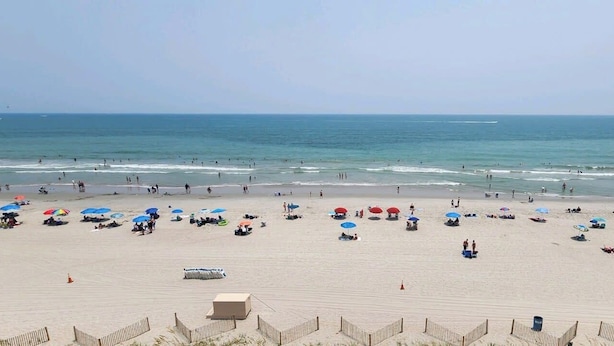 Uma praia com guarda-sóis, pessoas e céu claro.