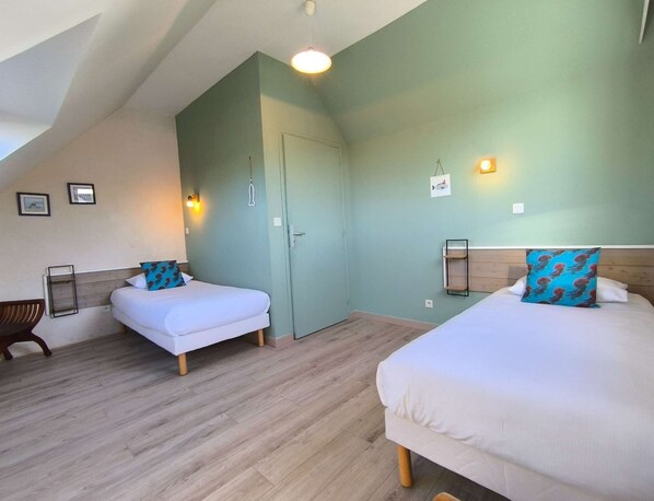 A room with two beds, a wooden floor, and a door.