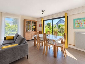 A modern living room with a grey sofa, a dining table with chairs, a wooden cabinet, and a large window with a view of greenery. - House La Roche Noire Erquy *Pool* *Beach at 800m* (Erquy)