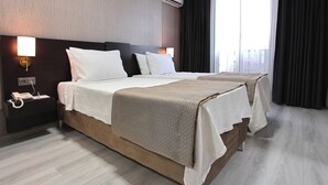 A hotel room with two beds, a bedside table with a phone, an air conditioner, and a window with curtains. - Mays Royal Hotel (Istanbul)