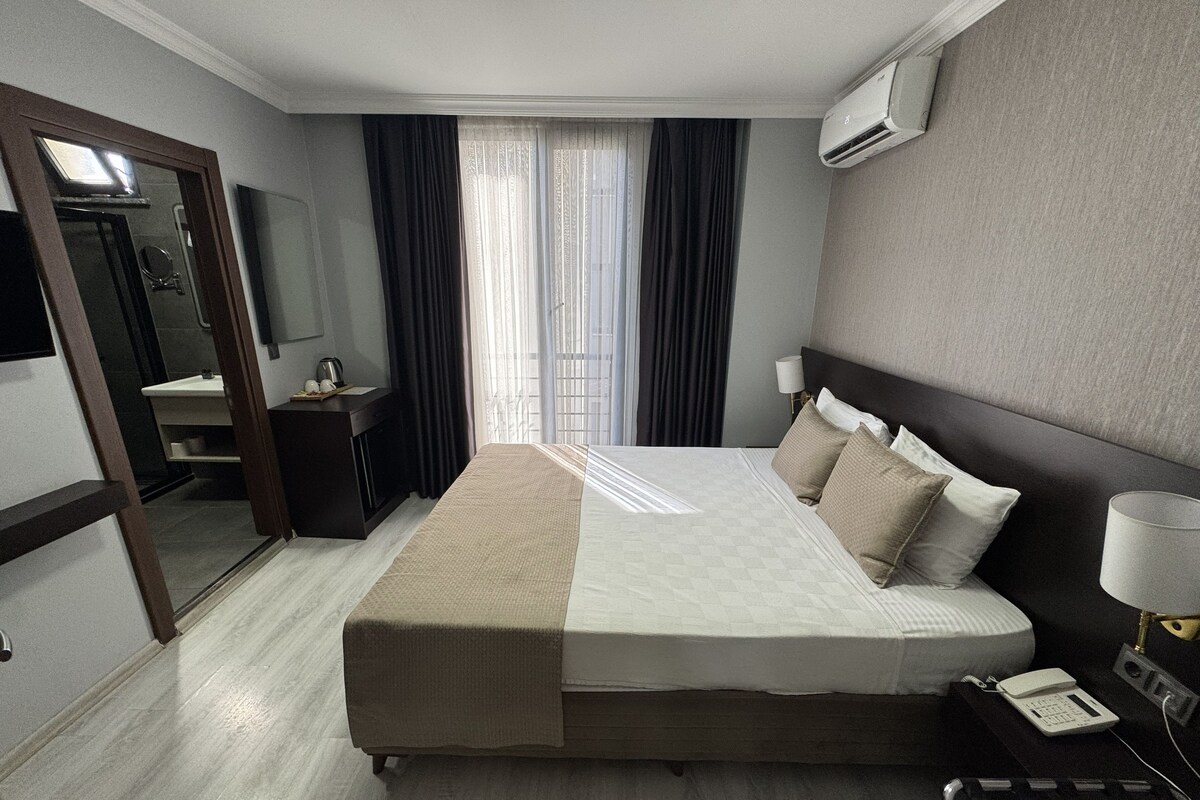 A hotel room with a bed, a bedside table, a lamp, a phone, and a mirror.