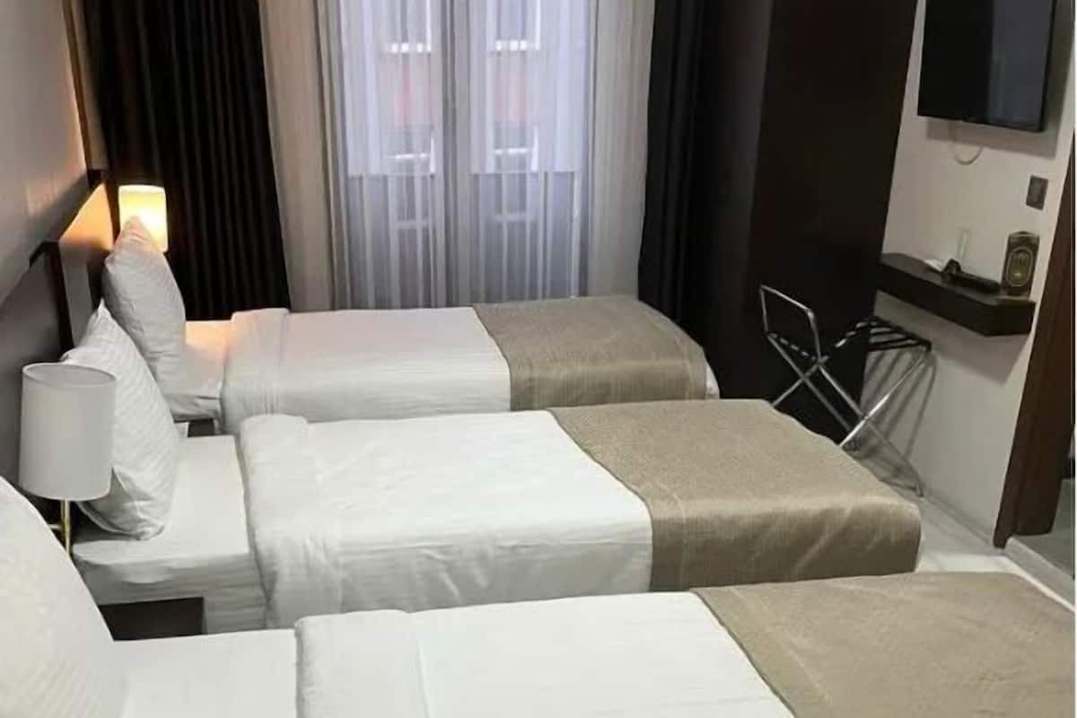 A hotel room with three beds, a TV on the wall, and a window with curtains.