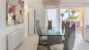 A modern dining area with a glass table, cushioned chairs, and a large abstract painting on the wall. - La Manga Club Los Olivos Apartment 600 (Atamaría)