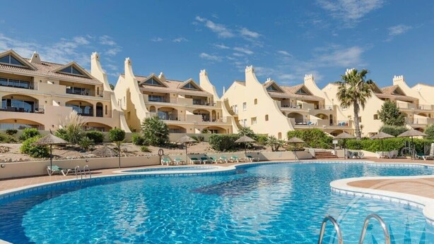 A resort with a large pool, multiple balconies, and palm trees. - La Manga Club Los Olivos Apartment 600 (Atamaría)