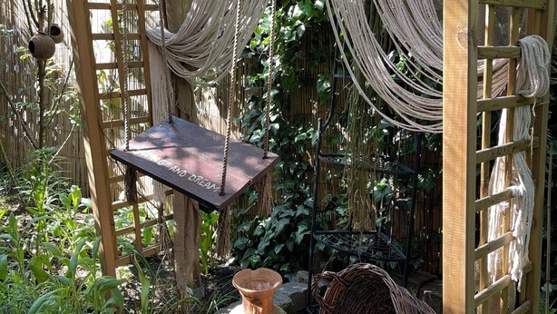 Un jardí amb una pèrgola de fusta, macramè penjat i testos de terracota.