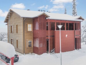 A two-story building with a wooden facade and a red section, surrounded by snow.