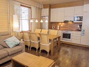 Una sala de estar acogedora con un sofá, una mesa de comedor con sillas, una mesa de centro de madera y una zona de cocina con armarios y electrodomésticos.
