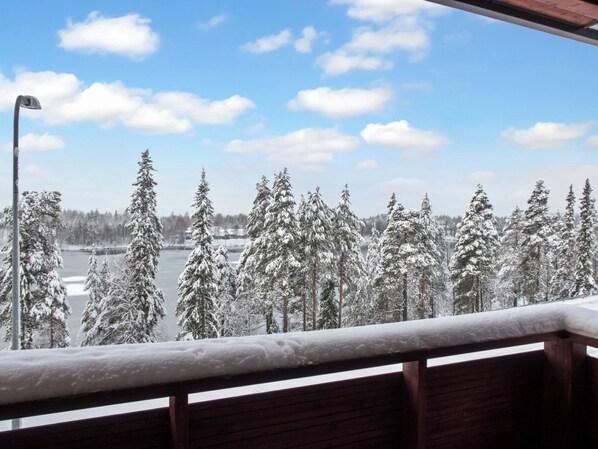 A snowy landscape with a clear sky, a wooden balcony railing, and snow-covered trees.