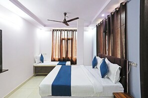 Una habitación de hotel con una cama grande, una cama más pequeña, un ventilador de techo y cortinas en la ventana.