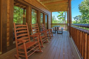 Une terrasse en bois avec des fauteuils à bascule et une table, donnant sur une zone boisée.