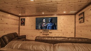 A cozy room with a large TV screen displaying a superhero movie, wooden walls, and leather seating.