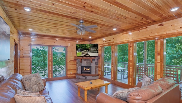 A wooden cabin interior with a stone fireplace, leather sofas, and large windows.