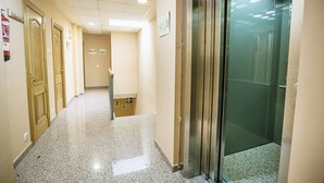 A hallway with a polished floor, wooden doors, and a glass elevator. - Hospedería Puerta de la Catedral (Ciudad Rodrigo)
