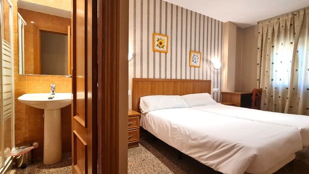 A hotel room with a wooden bed, a white sink, and striped wallpaper. - Hospedería Puerta de la Catedral (Ciudad Rodrigo)
