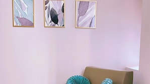 A beige armchair with two patterned pillows, a blue ottoman, and three abstract paintings on a light pink wall. - San Pietro Rooms 84 (Rome)