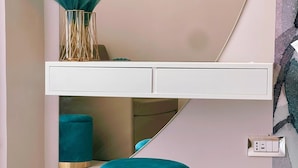 Una habitación moderna con una consola blanca, un otoman teal y arte abstracto en la pared.