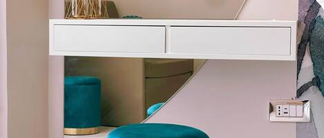 A modern room with a white console table, teal ottoman, and abstract wall art.