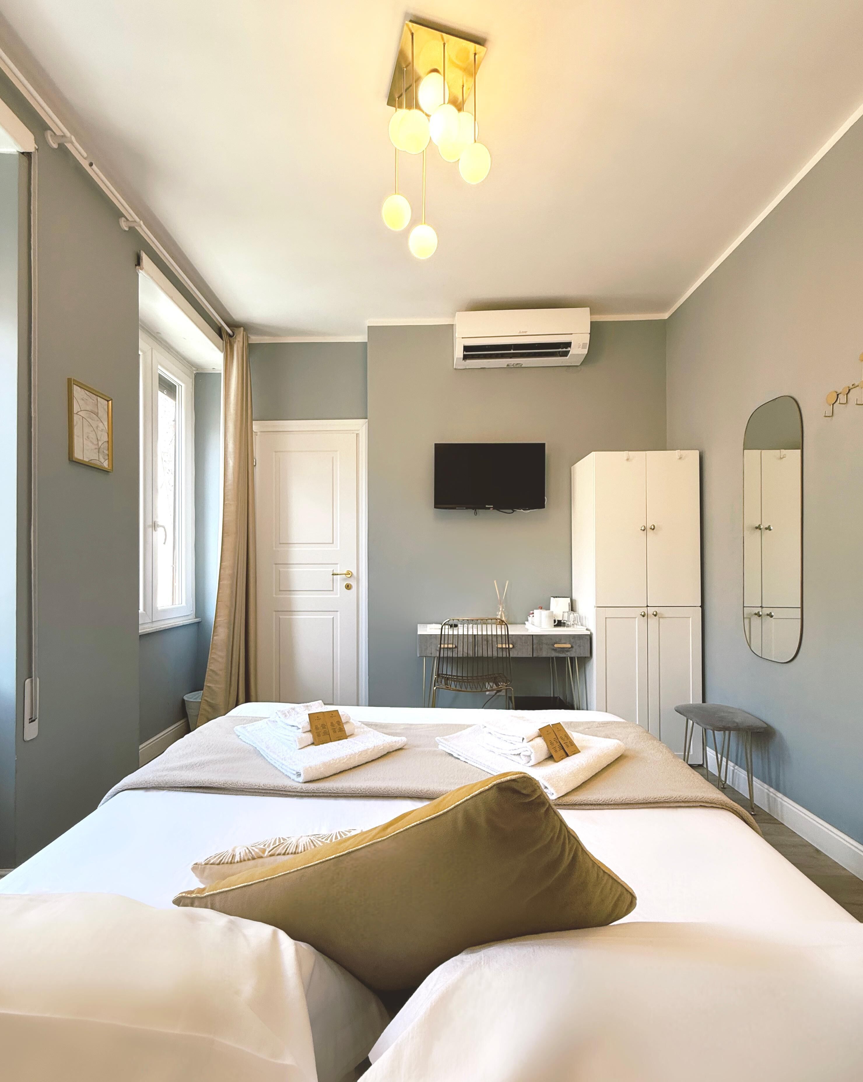 A hotel room with a bed, a desk, a chair, a TV, a wardrobe, and an air conditioning unit.
