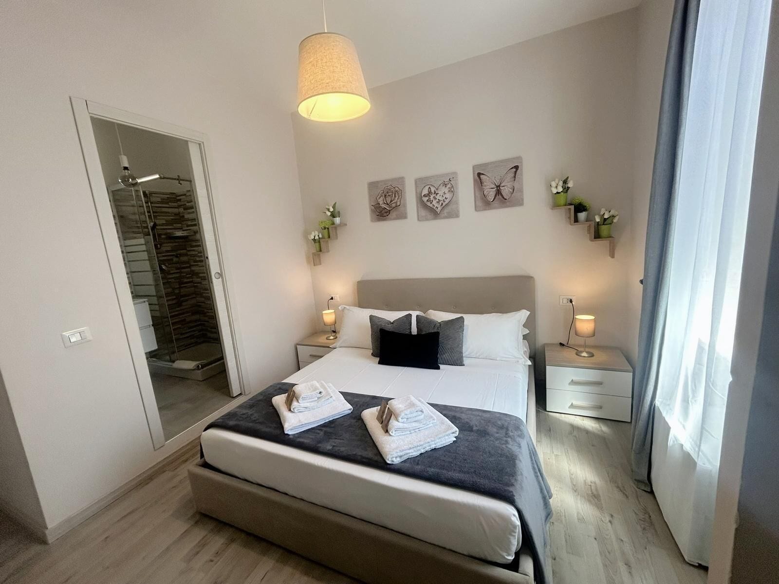 A modern bedroom with a large bed, bedside tables, a mirror, and artwork on the wall.