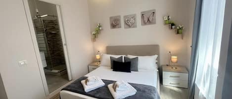 A modern bedroom with a large bed, bedside tables, a mirror, and artwork on the wall.