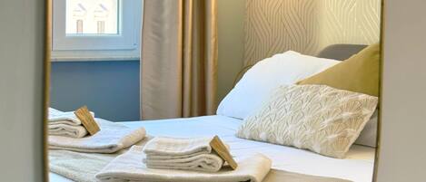 A hotel room with a bed, a mirror, a window, and a wall-mounted light fixture.