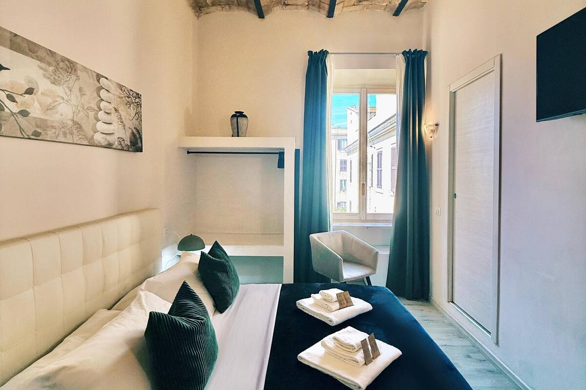 Ein Hotelzimmer mit Bett, Sessel, einem Gemälde und Blick auf die Straße.