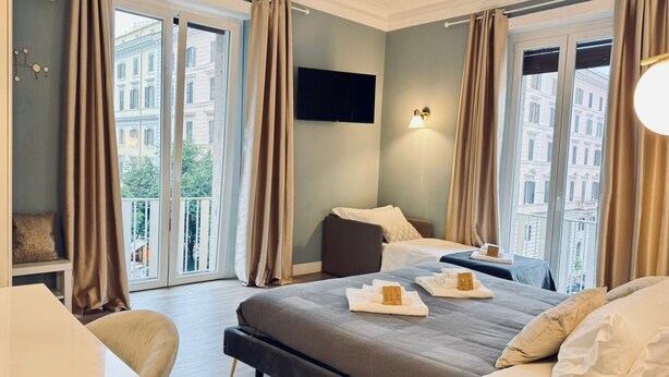 Habitación de hotel con una cama grande, un escritorio y una silla. Hay dos ventanas con cortinas y un televisor de pantalla plana montado en la pared.