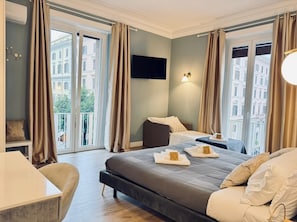 A hotel room with a large bed, a desk, and a chair. There are two windows with curtains, and a flat-screen TV mounted on the wall. - San Pietro Rooms 84 (Rome)