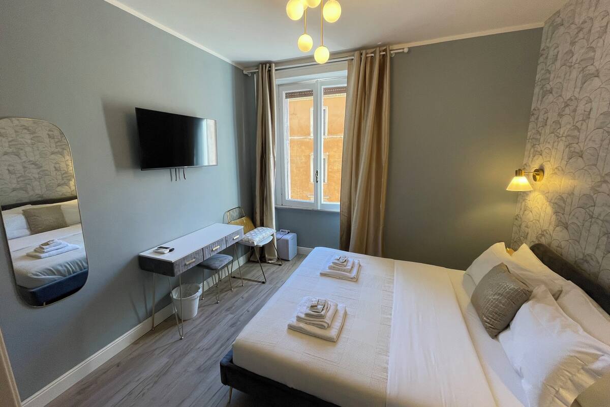 Ein Hotelzimmer mit Bett, Schreibtisch, Sessel, Fernseher und einem fensterbepflanzten Fenster.