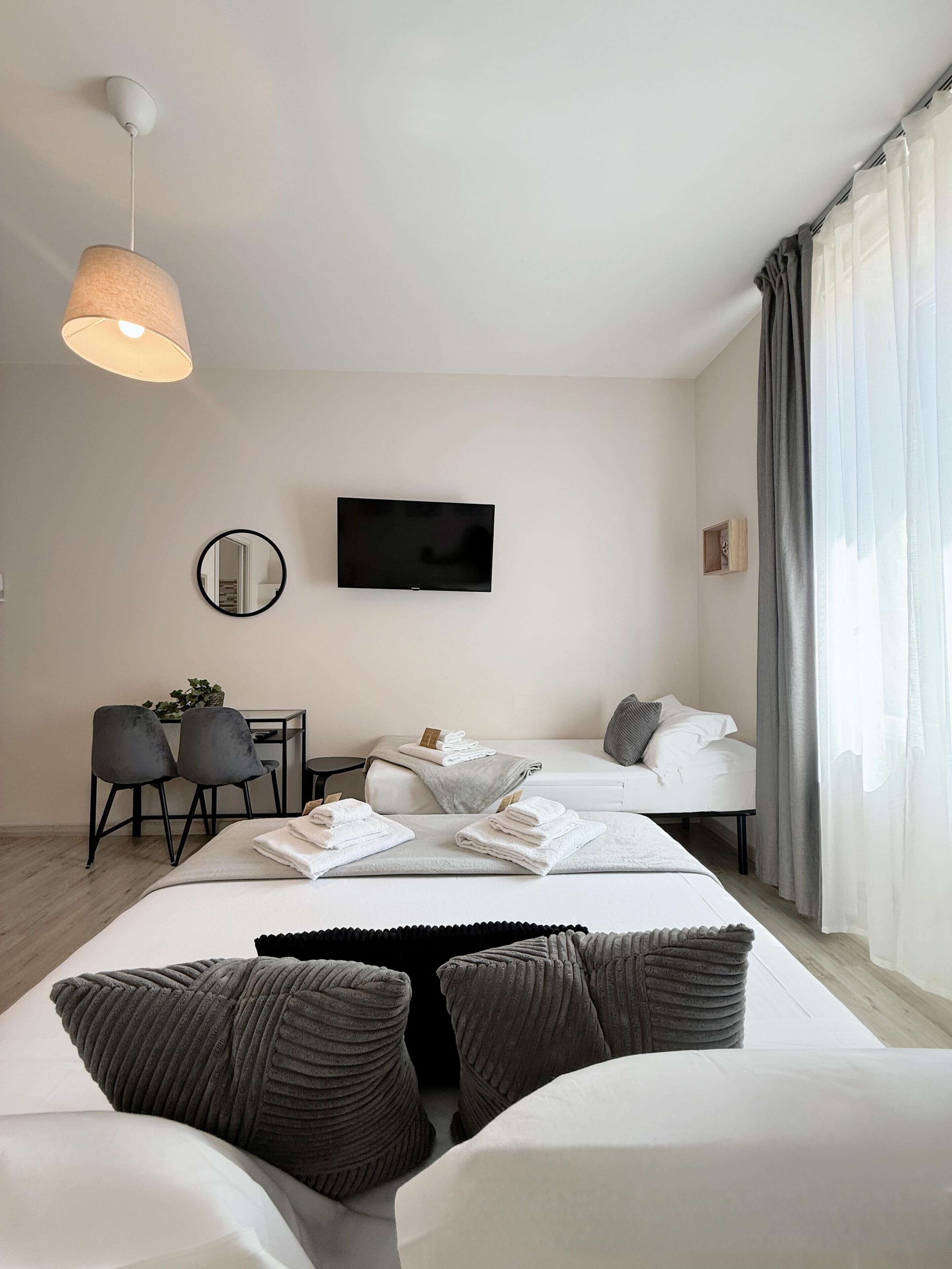 A modern hotel room with a bed, a desk, a chair, a TV, and a window with curtains.