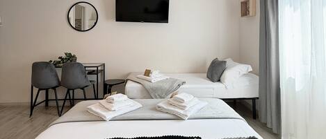 A modern hotel room with a bed, a desk, a chair, a TV, and a window with curtains.
