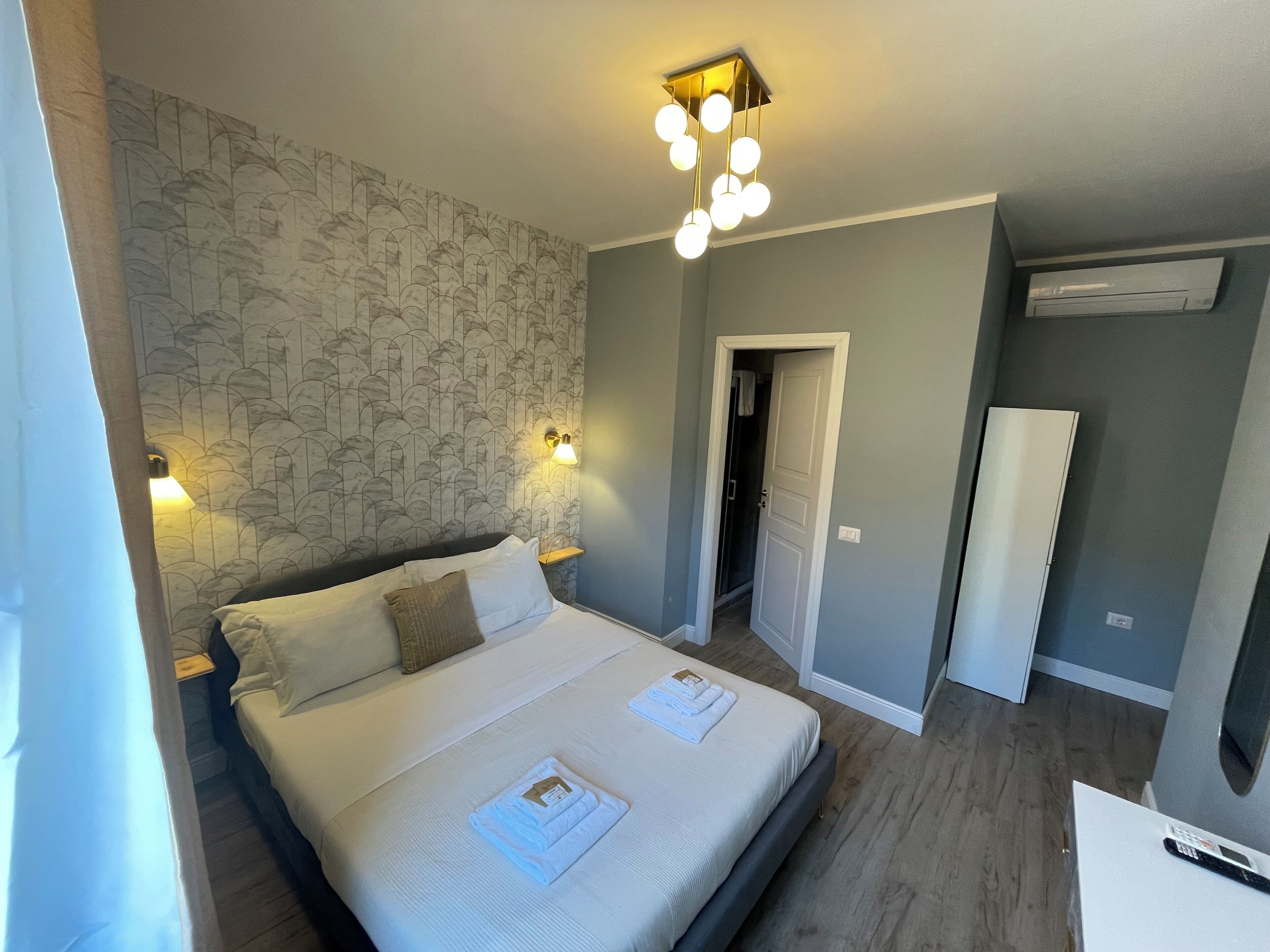Ein Hotelzimmer mit Bett, Nachttisch, Wandleuchte und Tür zu einem Badezimmer.
