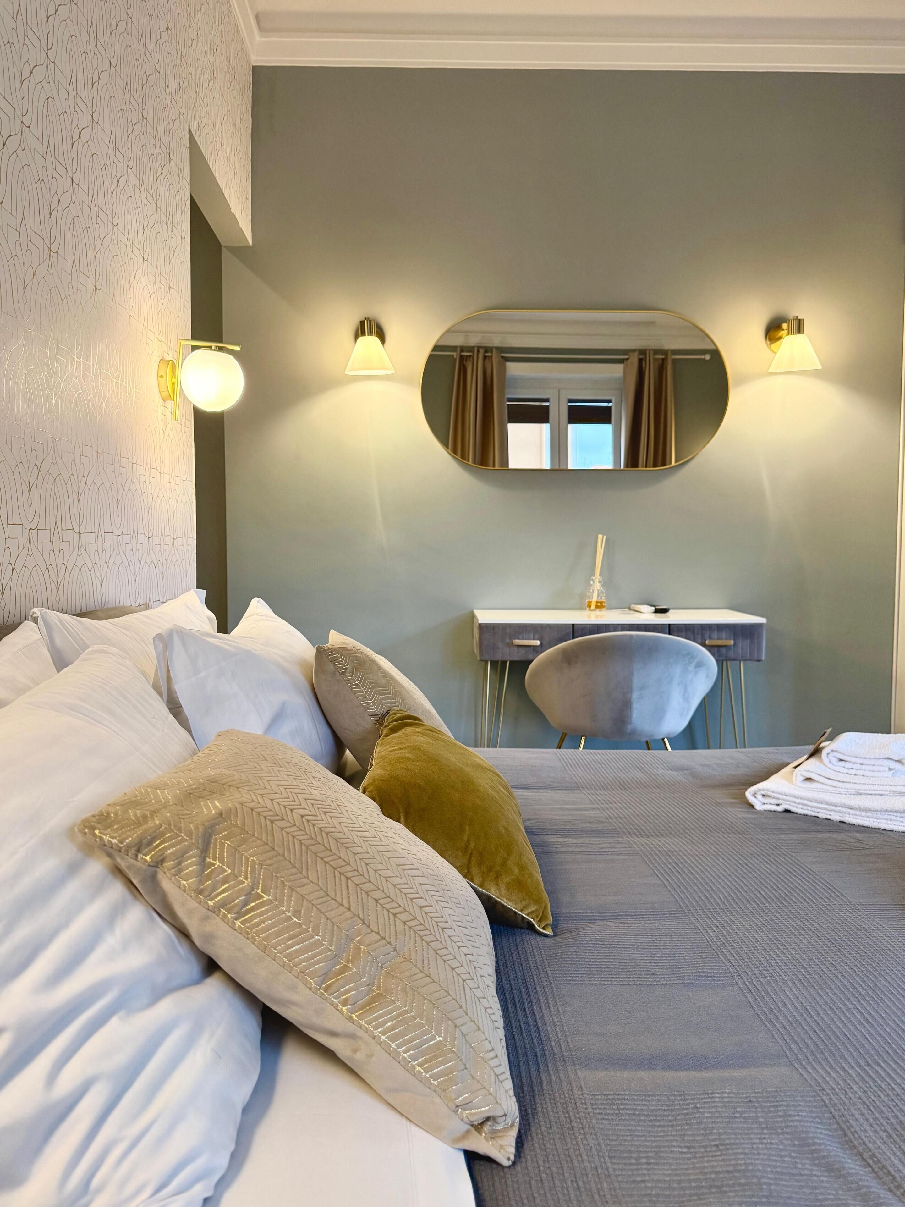 Hotellihuone, jossa on suuri sänky, peilillä varustettu työpöytä ja kaksi seinään kiinnitettyä valaisinta.