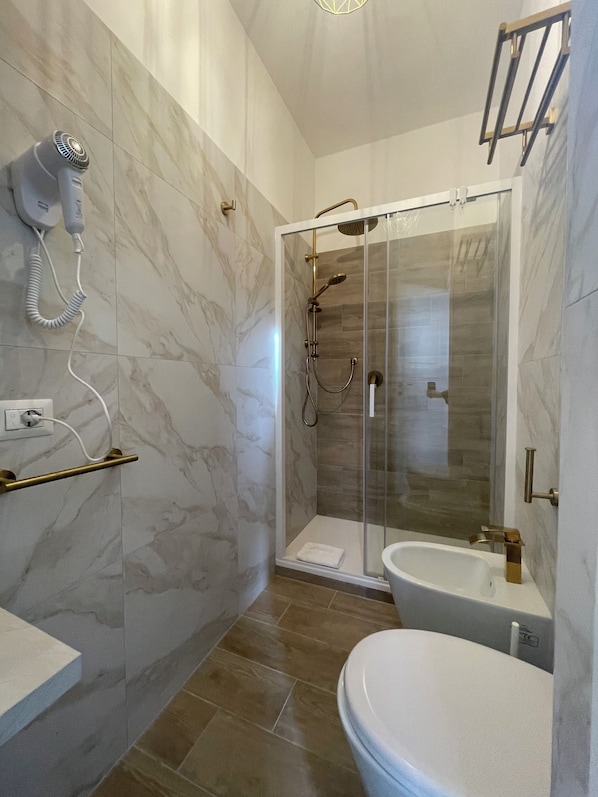 A modern bathroom with a glass-enclosed shower, a toilet, and a hairdryer mounted on the wall. - San Pietro Rooms 84 (Rome)