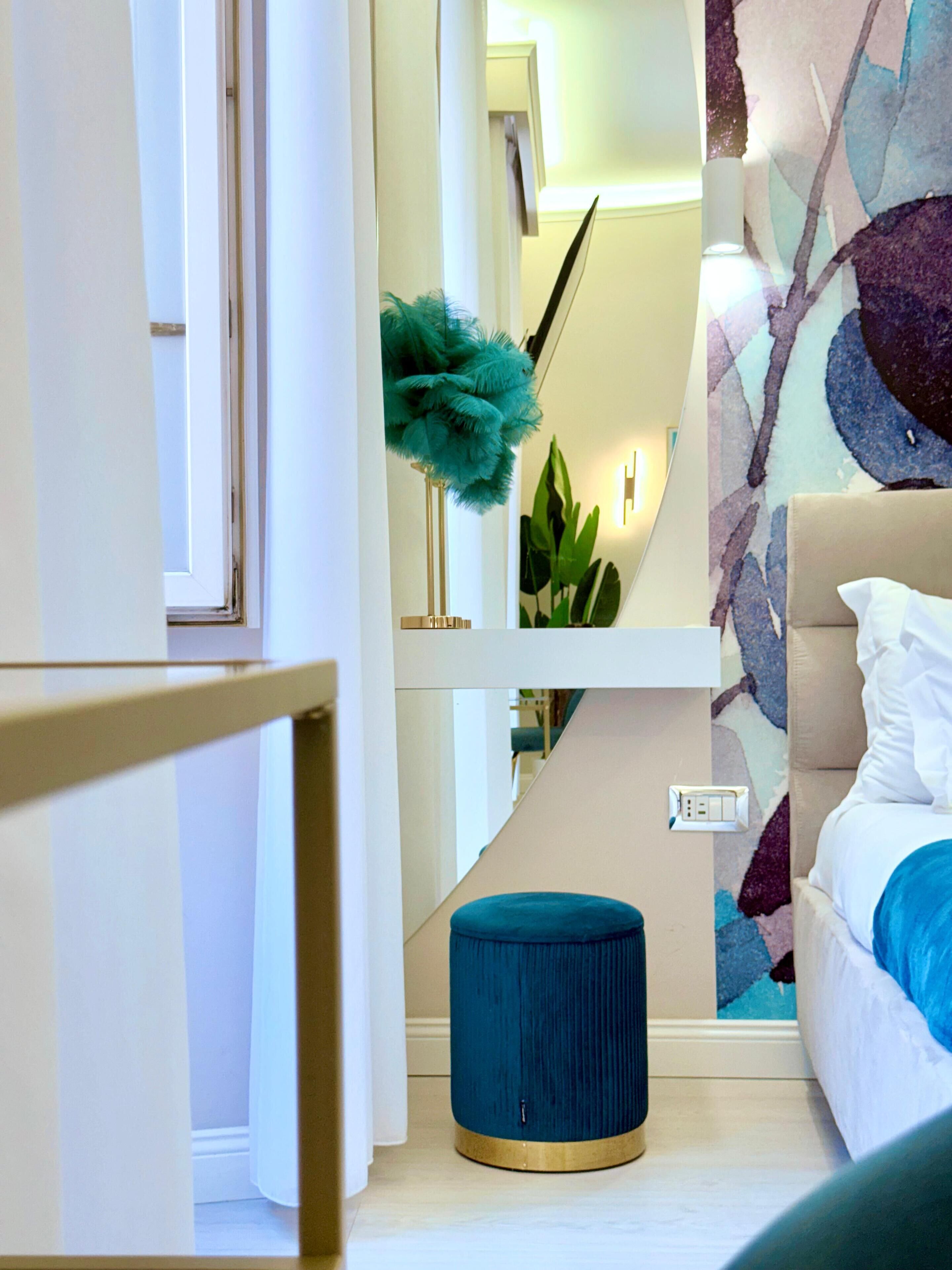 Une chambre à coucher avec un lit, un pouf bleu, un miroir et un mur orné d’œuvres d’art abstraites.