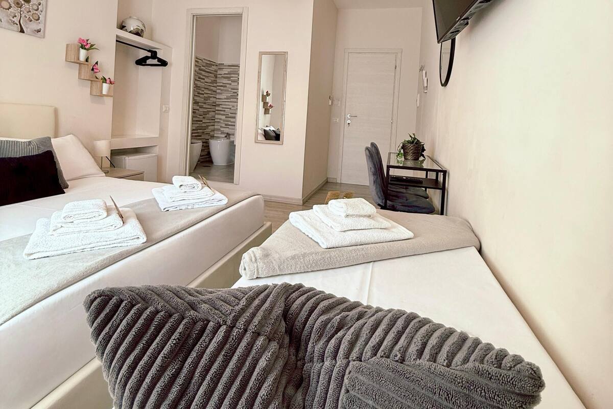 Ein Hotelzimmer mit zwei Betten, einem an der Wand befestigten Fernseher und einem kleinen Tisch mit einer Pflanze.