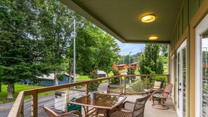 Un balcon agrémenté de meubles en osier, d’une table en verre et offrant une vue sur un lac et des bâtiments.