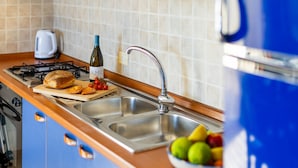 Une cuisine équipée d’une cuisinière à gaz, d’un évier et d’un plan de travail sur lequel se trouvent une miche de pain, des tomates et une bouteille de vin.