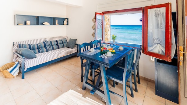 Une pièce comprenant un canapé, une table à manger, des chaises et donnant sur la mer.