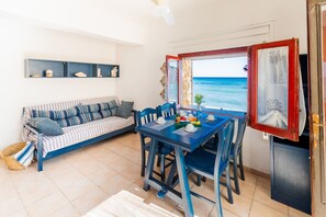 A room with a sofa, dining table, chairs, and a view of the sea. - Apollo's Terraces-Apartments on the beach less than 20 m from the sea!Libeccio (Marinella)